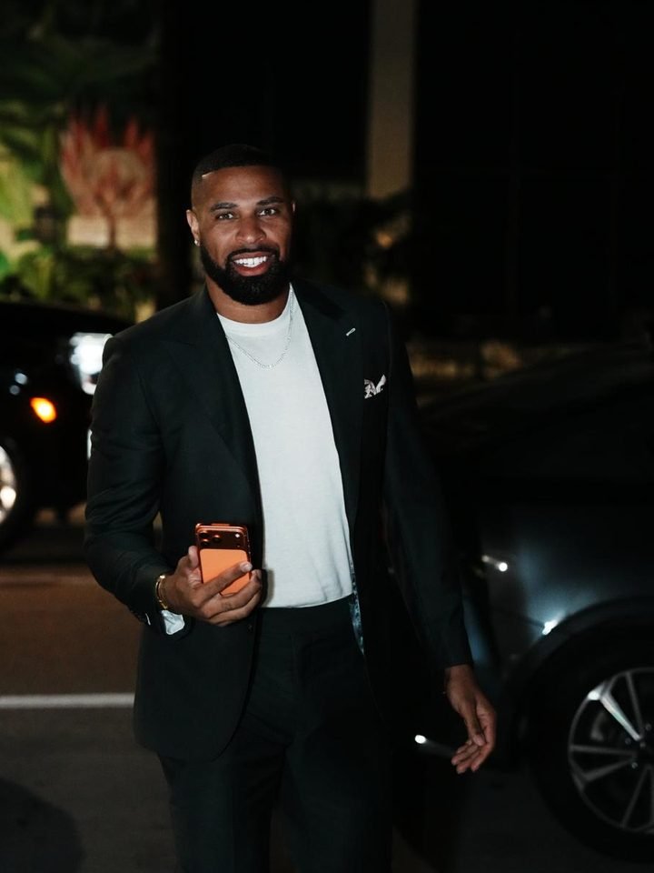 David, owner of DQG Prestige Enterprises, smiling outdoors at night in a dark suit, with parked cars behind him.